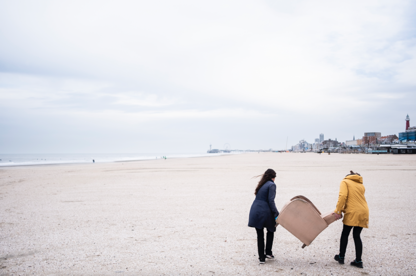 Strandjutten - twee deelnemers aan de workshop lopen met een in de duinen achtergelaten fauteuil over het strand van Scheveningen
