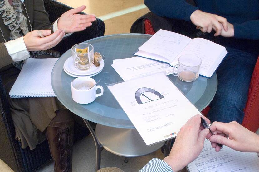 Drie mensen zitten rond een tafel met documenten