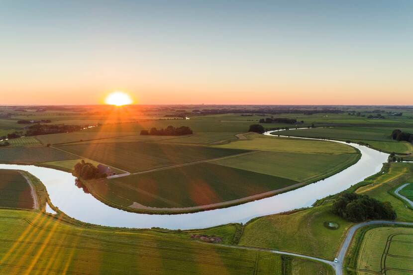 Een rivier slingert zich een weg door het vlakke land bij zonsopkomst.